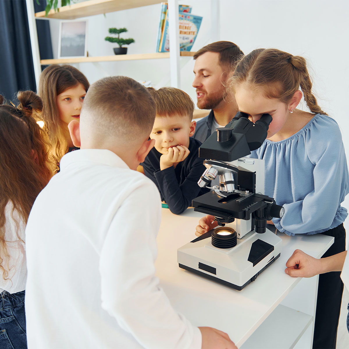 Working with the microscope. Group of children students in class at school with teacher.
